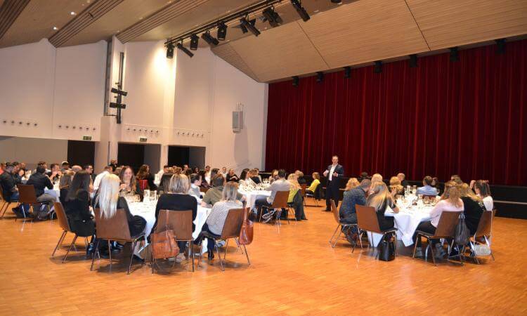 Rektor Stefan Kriz spricht zu den Anwesenden Saal mit runden Tischen und Menschen